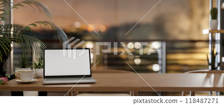 A laptop mockup on a wooden tabletop in a room by the window, offering a dusk view through a balcony 118487271