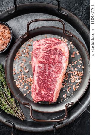Fresh Raw Wagyu striploin or New york steak in a steel tray with herbs. Black background. Top view 118487761