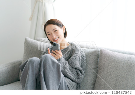 Woman sitting on sofa and using smartphone Woman sitting on sofa and using smartphone 118487842