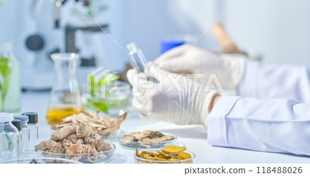 A scientist holds a small, empty, transparent vial in a modern laboratory setting filled with herbs and laboratory equipment needed for the experiment. A scientist holds a small, empty, transparent vial in a modern laboratory setting filled with herbs and laboratory equipment needed for the experiment. 118488026
