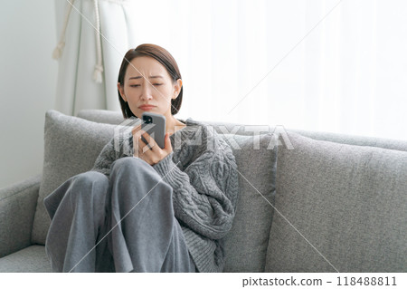 Woman sitting on sofa and using smartphone 118488811