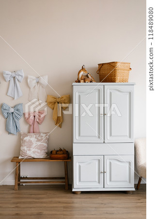 White dresser with bows hanging on the wall and straw basket on top in cozy and welcoming atmosphere children room 118489080