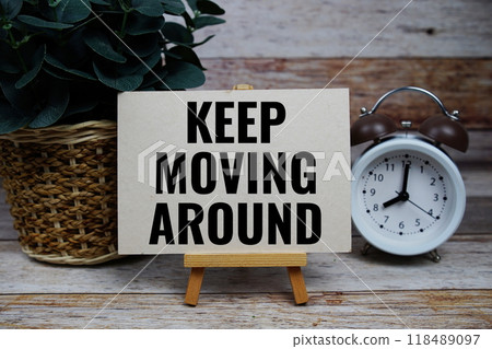 Keep Moving Around text on paper card with alarm clcok on wooden background Keep Moving Around text on paper card with alarm clcok on wooden background 118489097