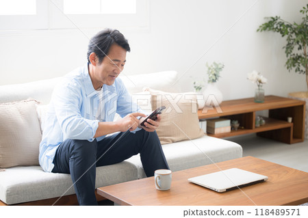 Full body of a senior man looking at his smartphone in a beautiful living room Full body of a senior man looking at his smartphone in a beautiful living room 118489571