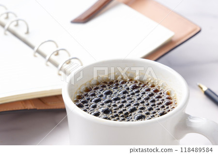 一張在辦公桌前工作、拿著咖啡、筆記本和原子筆的圖片。 118489584