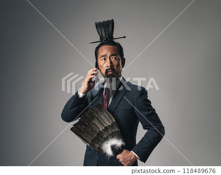 A scene of a historical Chinese military strategist, such as Zhuge Liang from the Romance of the Three Kingdoms, wearing a business suit and talking on a smartphone 118489676