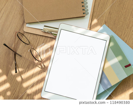 A workspace setup with a tablet, notebooks, glasses, and stationery on a wooden table 118490380