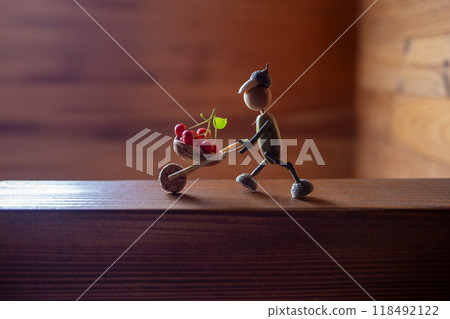 Handmade autumn figurine from acorns with twig limbs, acorn cap head, pushing berry-filled twig wheelbarrow, blue sky background, ideal for DIY craft, eco friendly kids activity, 118492122