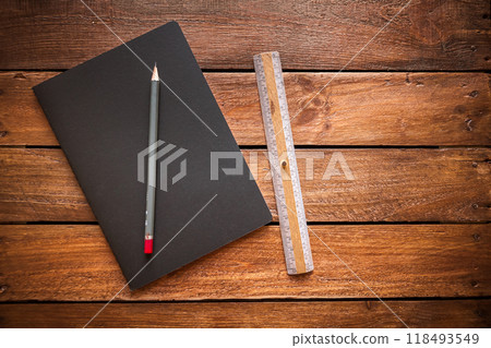 Closed notebook, pencil and old ruler on a rustic wooden board Closed notebook, pencil and old ruler on a rustic wooden board 118493549