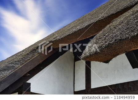 Thatched roof stands out against the white wall of a traditonal german under a clear blue sky with wispy clouds 118494959