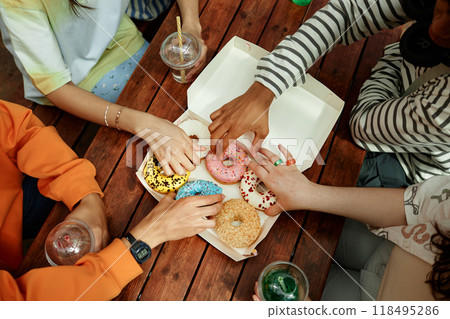 High angle shot of unrecognizable teenagers reaching for delicious sprinkled donut from takeaway box placed on cafe table while partying outdoors 118495286