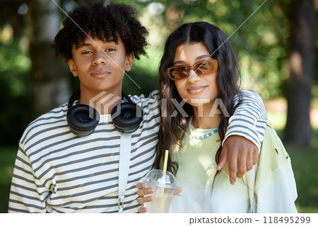 Portrait of African American teenage boy with headphones posing next to Middle Eastern girlfriend smiling for camera. Young couple enjoying summer day in park Portrait of African American teenage boy with headphones posing next to Middle Eastern girlfriend smiling for camera. Young couple enjoying summer day in park 118495299