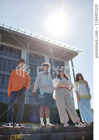 Vertical shot of cool teenagers standing on steps outside posing in group of four looking confidently into distance showcasing casual outfits for walk 118495320