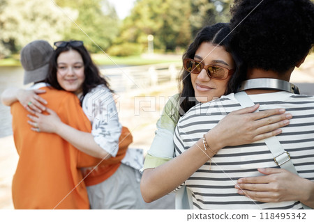 Smiling teenage girl with sunglasses giving young boy warm and friendly hug as couples meet outside to go for walk in park, copy space 118495342