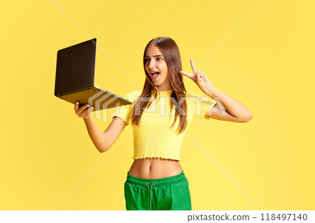 Young girl, student captured gesturing peace during meeting online in laptop against bright yellow background. Young girl, student captured gesturing peace during meeting online in laptop against bright yellow background. 118497140