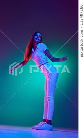 Artistic young girl, dressed total-white casual clothes and posing in neon light against gradient studio background. 118497160
