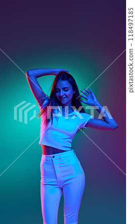 Young stylish dressed girl, joyful dancing in mixed neon lights against gradient studio background. Energetic moves. Young stylish dressed girl, joyful dancing in mixed neon lights against gradient studio background. Energetic moves. 118497185