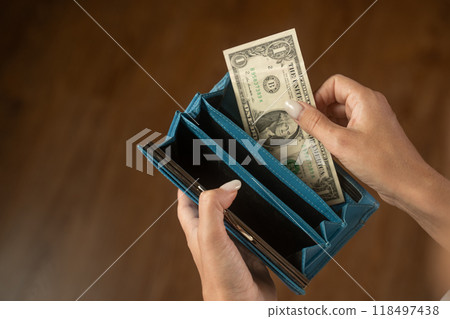 Woman putting one dollar bill in blue wallet 118497438