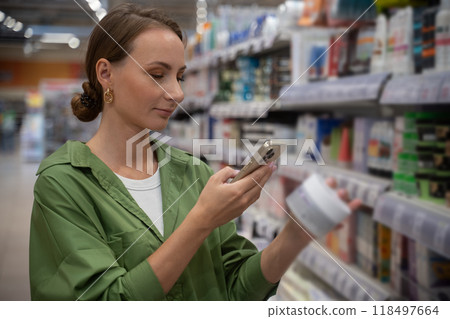 Young woman using smartphone scanning cosmetics product in supermarket 118497664
