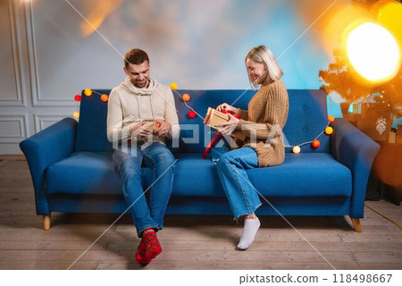 Young couple exchanging Christmas gifts sitting on sofa at home. Young couple exchanging Christmas gifts sitting on sofa at home. 118498667