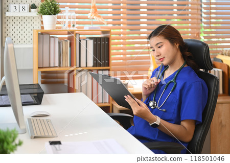 Smiling female doctor in a blue scrubs reviewing document in medical office Smiling female doctor in a blue scrubs reviewing document in medical office 118501046