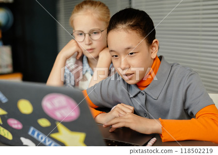 Portrait of concentrated Central Asian girl using laptop in class while browsing information and watching educational videos together with classmate at school, copy space 118502219
