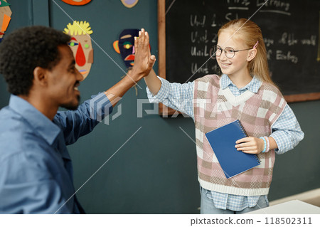 Medium shot of cheerful young female student high fiving male teacher while receiving praise for excellent job during lesson at primary school, copy space Medium shot of cheerful young female student high fiving male teacher while receiving praise for excellent job during lesson at primary school, copy space 118502311