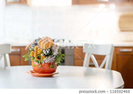 Thanksgiving day table setting decoration creative bouquet centerpieces with orange flowers in pumpkin as vase in modern home kitchen interior. Close up. 118502468