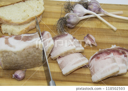 A knife cutting the salo on pieces. Ukrainian products raw lard with peppercorn and garlic, knife, slices of bread, salo lying on wooden board. Ukrainian traditional food concept. A knife cutting the salo on pieces. Ukrainian products raw lard with peppercorn and garlic, knife, slices of bread, salo lying on wooden board. Ukrainian traditional food concept. 118502503