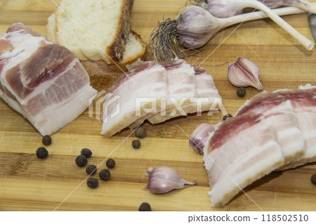 Ukrainian products raw lard with peppercorn and garlic, knife, slices of bread, salo lying on wooden board. Ukrainian traditional food concept. Ukrainian products raw lard with peppercorn and garlic, knife, slices of bread, salo lying on wooden board. Ukrainian traditional food concept. 118502510