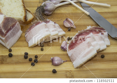 Ukrainian products raw lard with peppercorn and garlic, knife, slices of bread, salo lying on wooden board. Ukrainian traditional food concept. Ukrainian products raw lard with peppercorn and garlic, knife, slices of bread, salo lying on wooden board. Ukrainian traditional food concept. 118502511