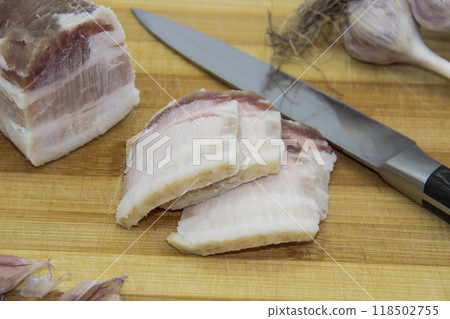 Ukrainian products raw lard with peppercorn and garlic, knife, slices of salo being on cutting board. Ukrainian traditional food concept. Ukrainian products raw lard with peppercorn and garlic, knife, slices of salo being on cutting board. Ukrainian traditional food concept. 118502755