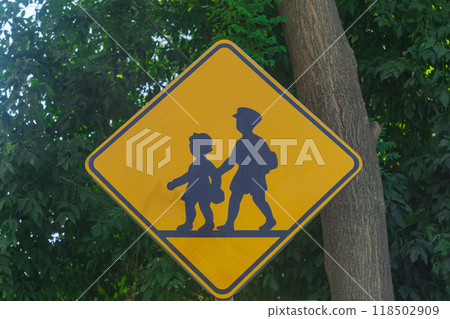 Yellow road sign with silhouettes of pedestrian children marked on it, signaling that there is a school nearby and there is a danger of children suddenly running out onto the roadway. 118502909