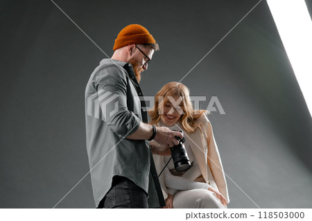 The photographer is displaying the camera screen to a joyful model in a photoshoot session 118503000
