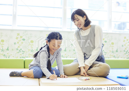A female childcare worker provides guidance to children as they draw. A female childcare worker provides guidance to children as they draw. 118503031