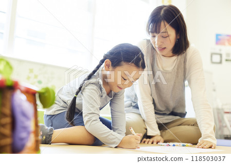 一位幼稚園女老師正在和正在畫畫的孩子說話。 一位幼稚園女老師正在和正在畫畫的孩子說話。 118503037