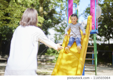 孩子在溜滑梯上玩耍，一名女性保育員在照顧她 118503064