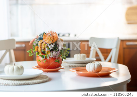 Thanksgiving day table setting decoration with creative bouquet centerpieces orange flowers in pumpkin as vase in modern home kitchen interior. Close up. Thanksgiving day table setting decoration with creative bouquet centerpieces orange flowers in pumpkin as vase in modern home kitchen interior. Close up. 118503243