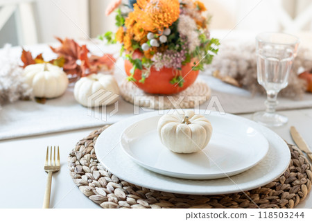Thanksgiving day table setting with candles, fall decorations, centerpiece of dry flowers and pumpkin on white table in modern kitchen. Close up. Thanksgiving day table setting with candles, fall decorations, centerpiece of dry flowers and pumpkin on white table in modern kitchen. Close up. 118503244