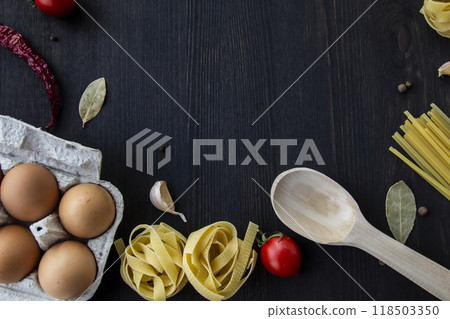 Cooking food background with free space for text. Composition with spaghetti, tomato, eggs, garlic, bay leaf over the wood background. Ingredients for cooking with copy space. Top view for the design 118503350