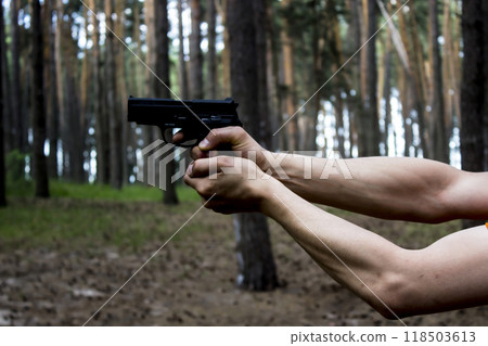 Strong Men's hands hold a gun against forest background. Danger situation in the forest Strong Men's hands hold a gun against forest background. Danger situation in the forest 118503613