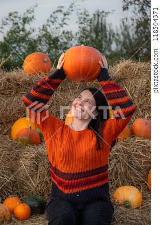 Woman holding a pumpkin sitting on hay bales Woman holding a pumpkin sitting on hay bales 118504371