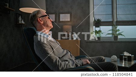 Portrait of a thoughtful adult psychologist sitting in a chair in his office and looking out the window at the sunset Portrait of a thoughtful adult psychologist sitting in a chair in his office and looking out the window at the sunset 118504841