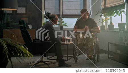 Military man in wheelchair discusses progress in therapy and shakes hands with psychotherapist 118504945