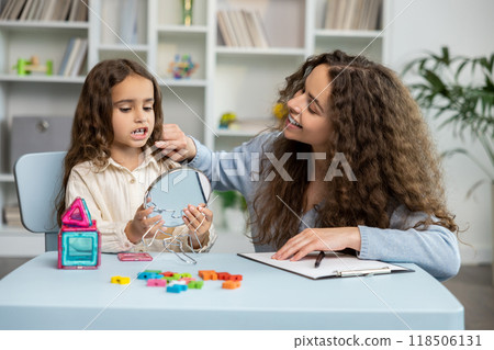 Cute long-haired girl exercising with a mirror at the speech therapist office 118506131