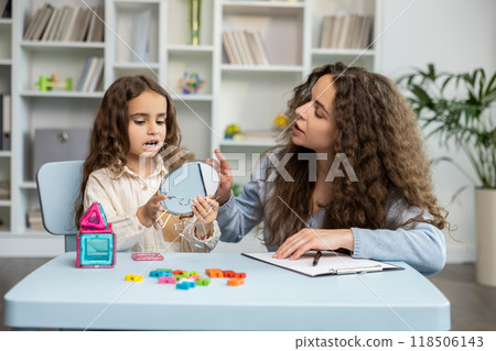Cute long-haired girl exercising with a mirror at the speech therapist office 118506143