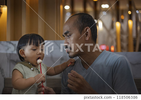 Father teaches toddler baby to eat meatball. Father and son are eating together in the restaurant. 118506386