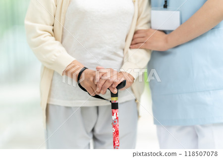 Senior woman with a walking stick and the hands of a caregiver Senior woman with a walking stick and the hands of a caregiver 118507078