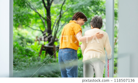 A woman walking while supporting an elderly woman, back view A woman walking while supporting an elderly woman, back view 118507136