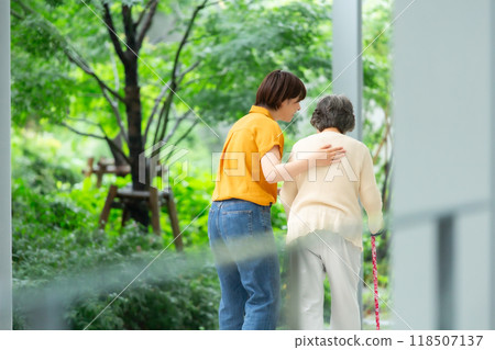 A woman walking while supporting an elderly woman, back view A woman walking while supporting an elderly woman, back view 118507137